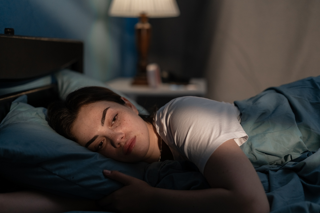 Young sad woman lying in bed late at night trying to sleep suffering insomnia. Girl in bed scared on nightmares looking worried and stressed. Sleeping disorder and insomnia